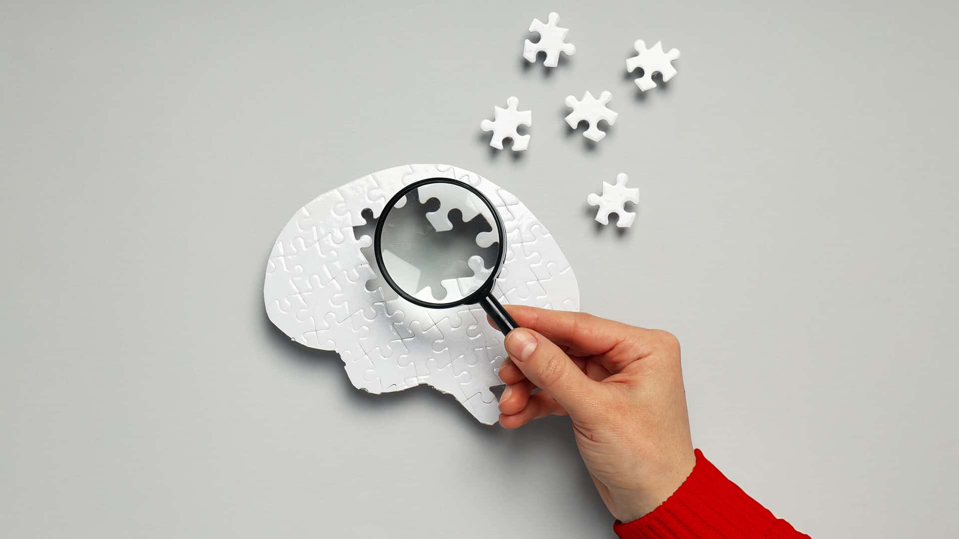 hand holding a small magnifying glass over a brain-shaped puzzle