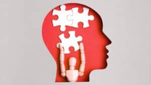 paper cutout of a human head shape, underneath are three puzzle pieces, one of which is being "held" by a wooden figure